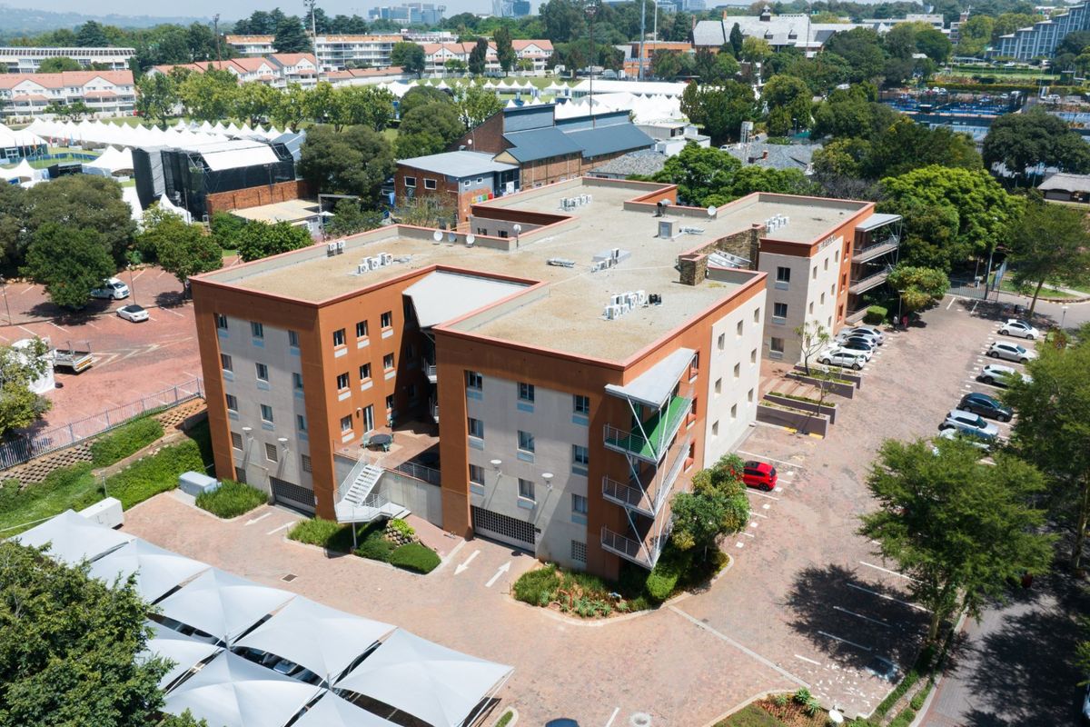 Aerial view of a multi-story commercial building featuring a flat roof, external staircases, balconies, and an extensive paved parking area.