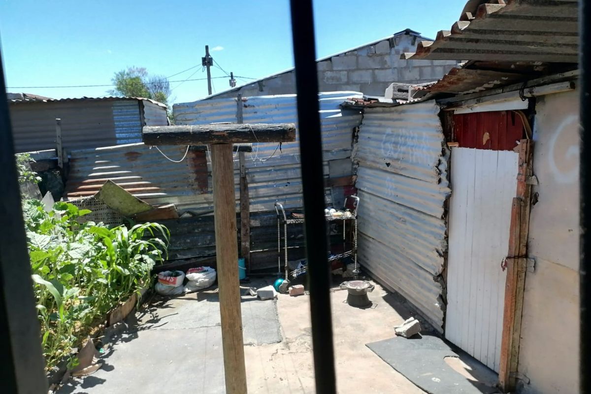 A rear outdoor area featuring corrugated iron fencing, concrete paving, and a timber post, showing significant signs of wear and structural deterioration.
