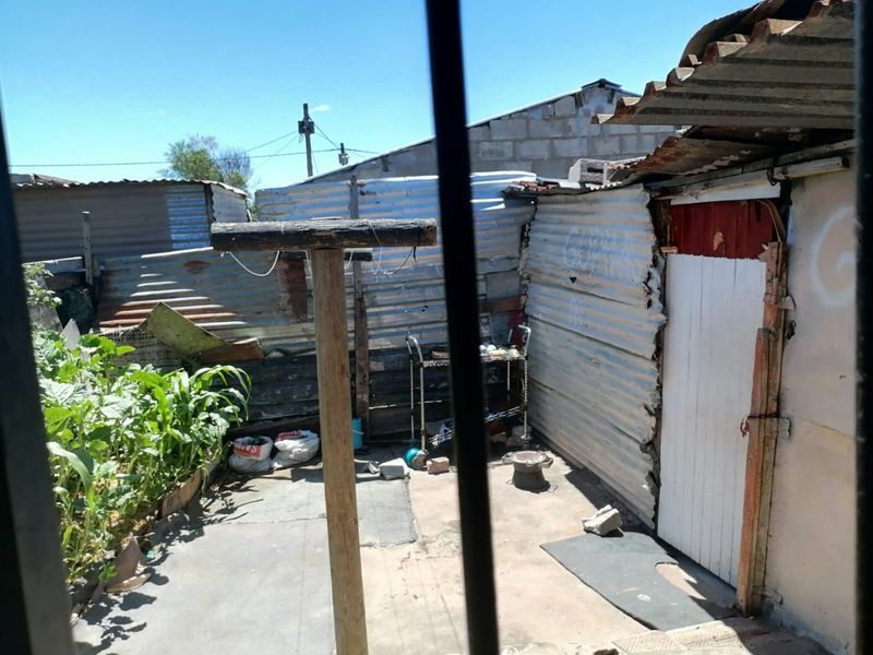 A rear outdoor area featuring corrugated iron fencing, concrete paving, and a timber post, showing significant signs of wear and structural deterioration.