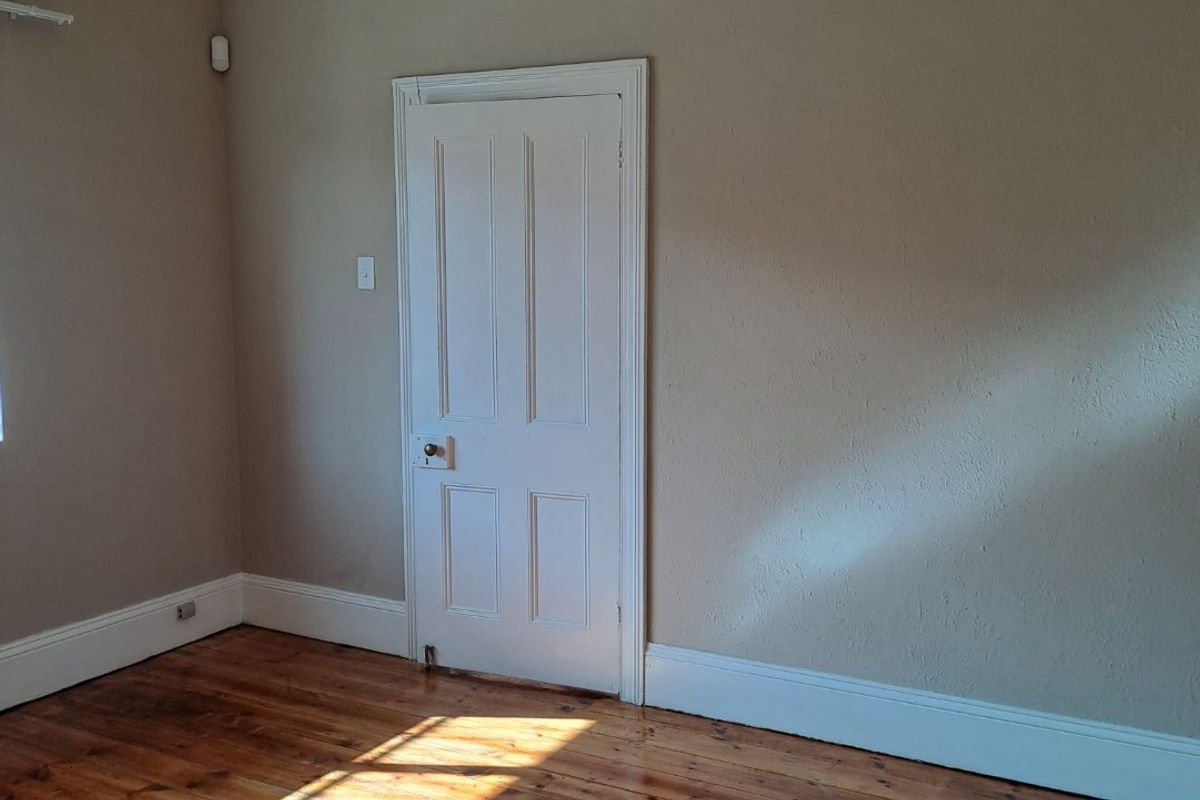 An empty bedroom featuring polished timber flooring, neutral wall tones, and a classic internal door.