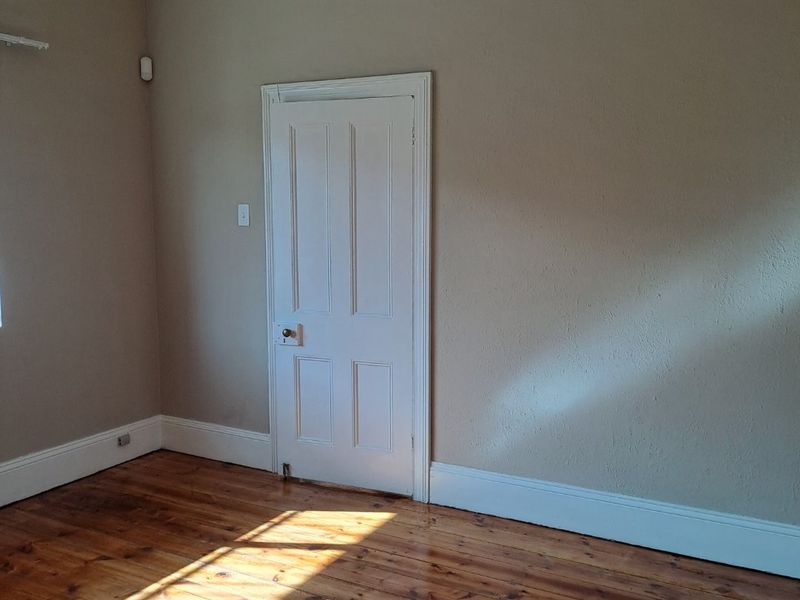 An empty bedroom featuring polished timber flooring, neutral wall tones, and a classic internal door.
