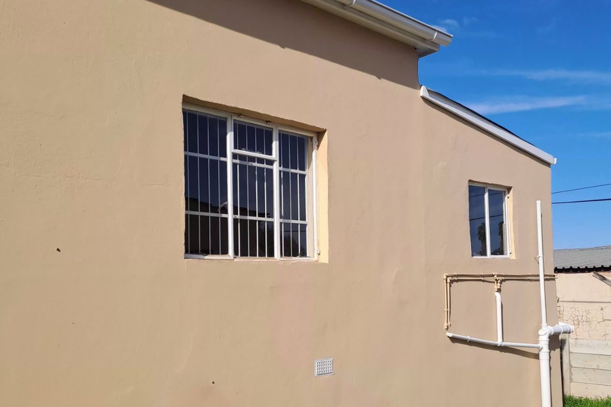 A view of the rear exterior wall featuring security bars on the windows, gutters, and external plumbing fixtures.
