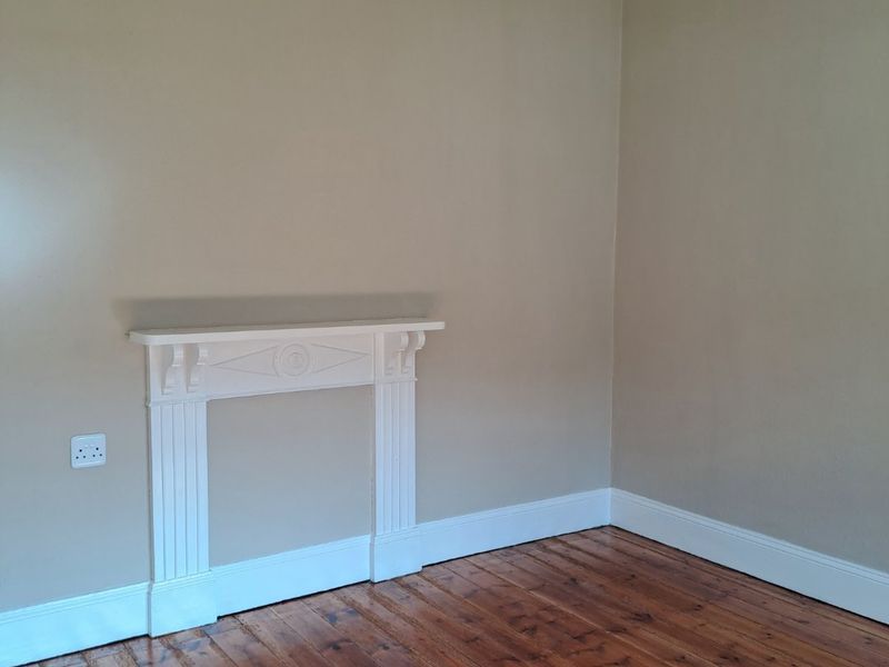 A bright, empty living room featuring polished timber flooring, neutral wall tones, and a classic decorative fireplace mantel.