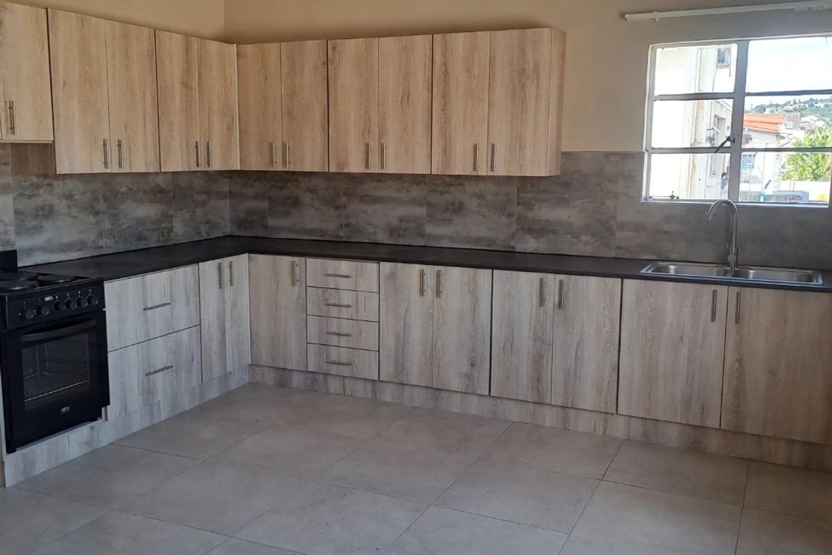 A clean, modern kitchen featuring light wood-grain cabinetry, dark countertops, tiled backsplash, and integrated oven, offering a functional and well-maintained workspace.