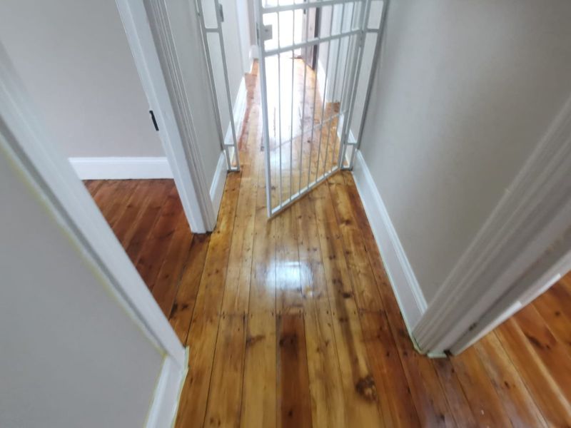 A bright hallway featuring polished timber flooring and a white security gate, connecting various rooms within the home.