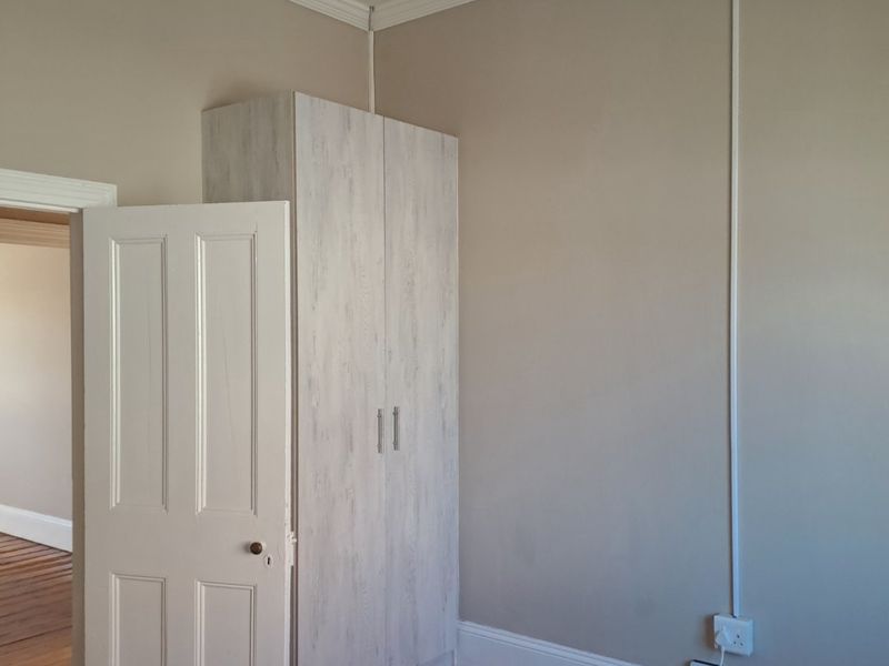 A bedroom featuring timber flooring, a built-in wardrobe, and classic architectural details including cornice and skirting boards.