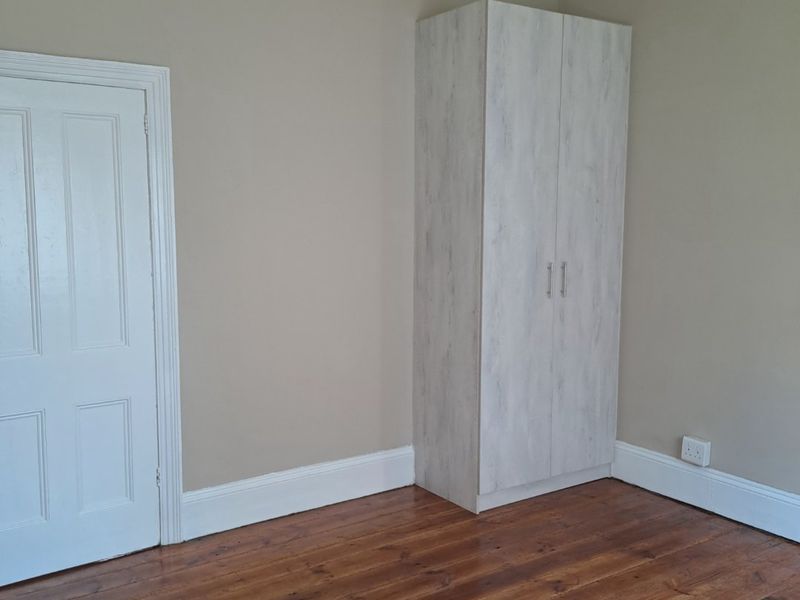 A clean, empty bedroom featuring polished timber flooring, neutral wall tones, and a modern built-in wardrobe.