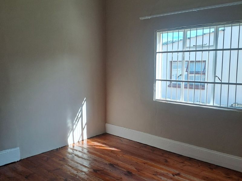 A vacant bedroom featuring polished timber flooring, neutral wall tones, and a window fitted with security bars.