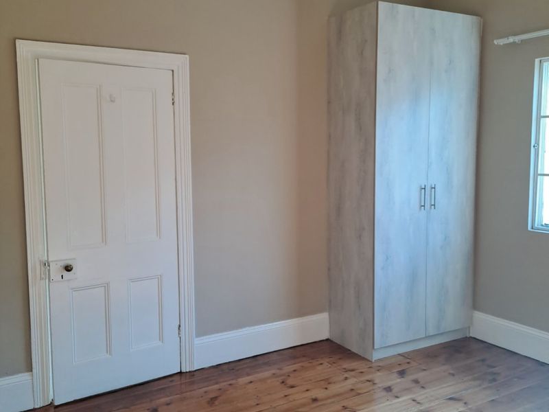 A bright, empty bedroom featuring polished timber flooring, neutral wall tones, and a modern built-in wardrobe.