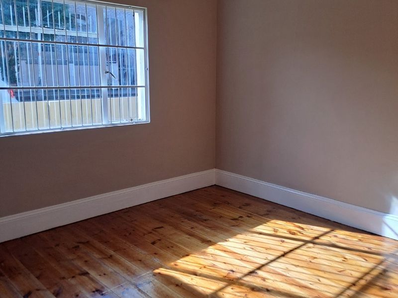 A bright, empty bedroom featuring polished timber flooring, neutral wall tones, and a window fitted with security bars.