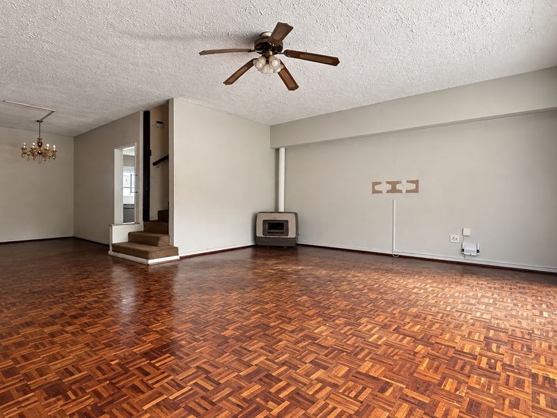 Spacious living area featuring original parquet flooring, a ceiling fan, and a freestanding fireplace, with direct access to the exterior through glass sliding doors.
