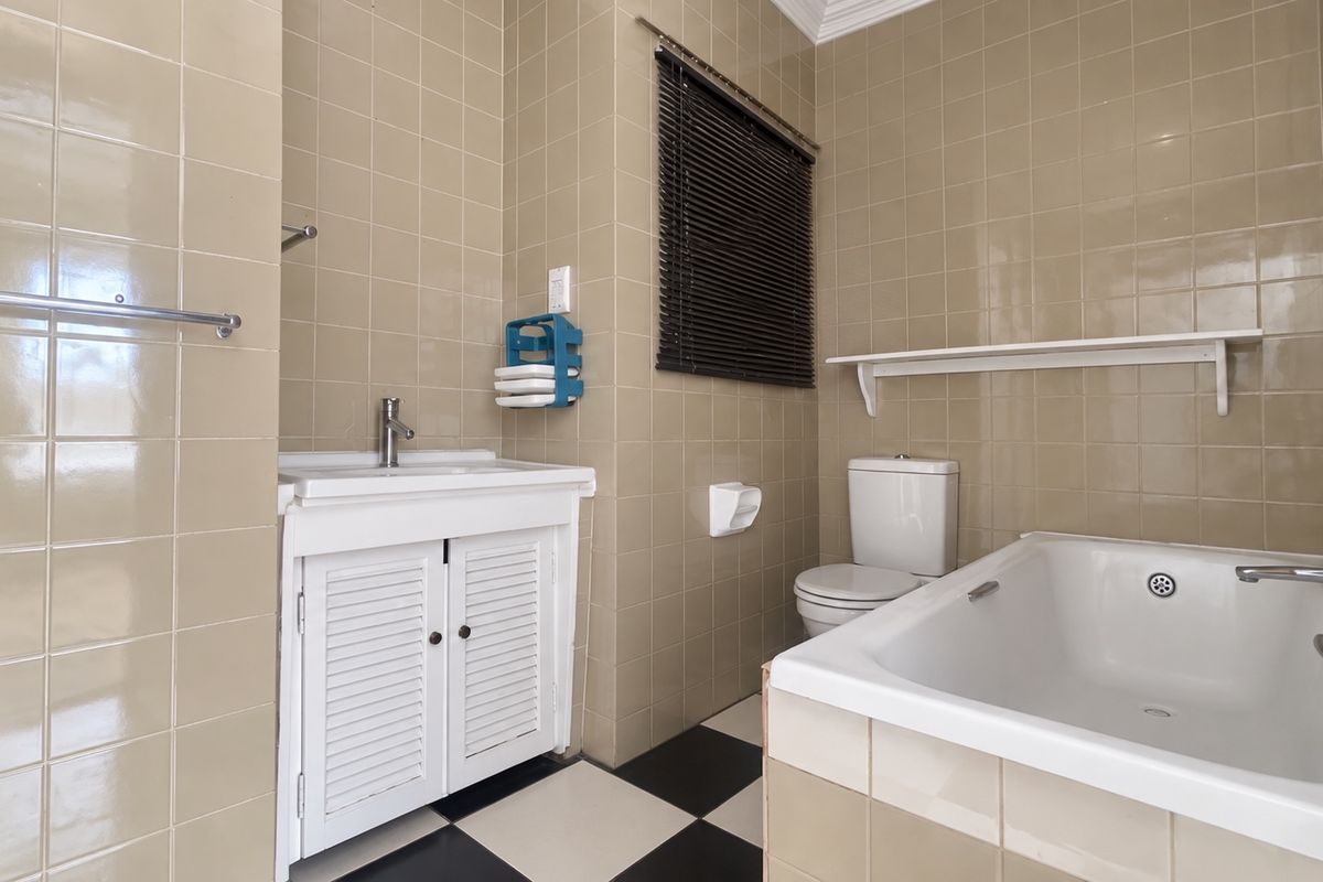 A functional bathroom featuring a vanity basin, toilet, and bathtub with full-height wall tiling and a classic black and white checkered floor.