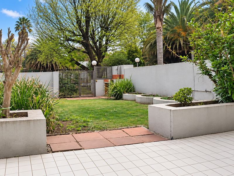 A private rear garden featuring a tiled patio area, built-in concrete planter boxes, a small lawn, and a secure metal pedestrian gate.