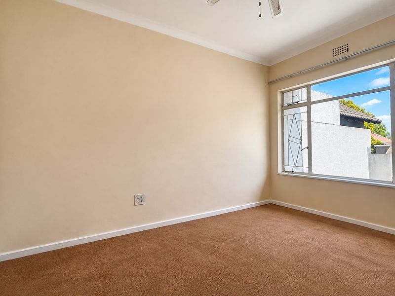 A vacant bedroom featuring neutral walls, carpet flooring, a built-in wardrobe, and a large window with security bars.