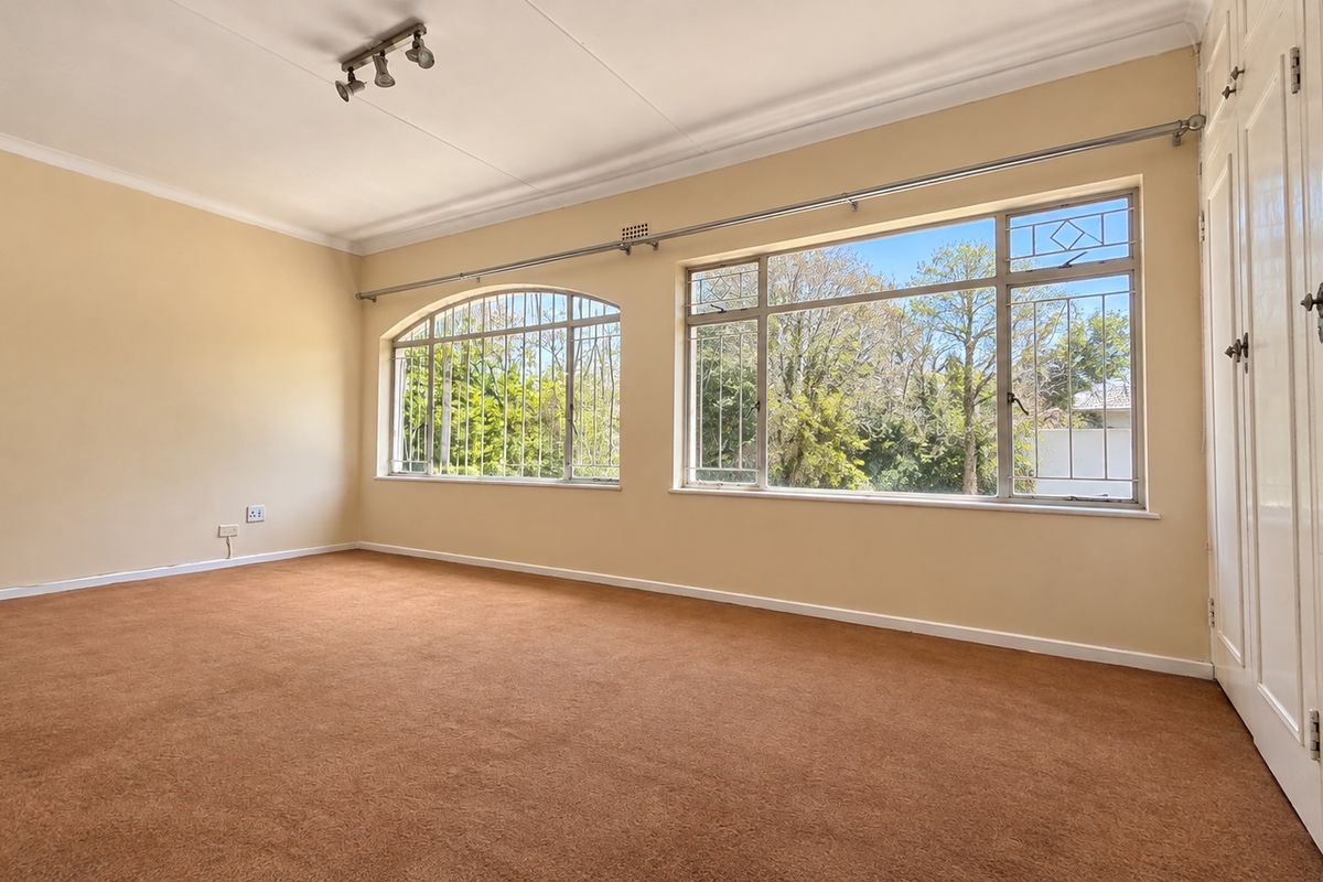 Spacious bedroom featuring built-in cupboards, large windows with security bars, and neutral wall finishes, offering a blank canvas for personalization.