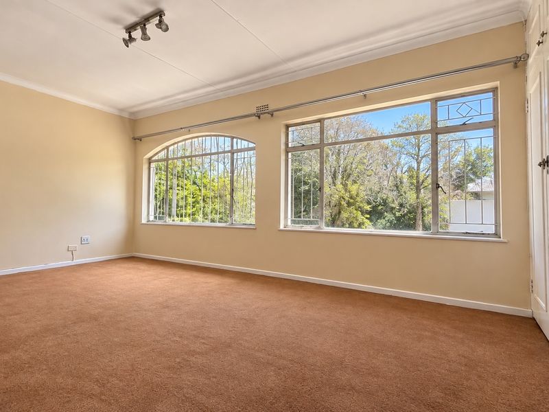 Spacious bedroom featuring built-in cupboards, large windows with security bars, and neutral wall finishes, offering a blank canvas for personalization.