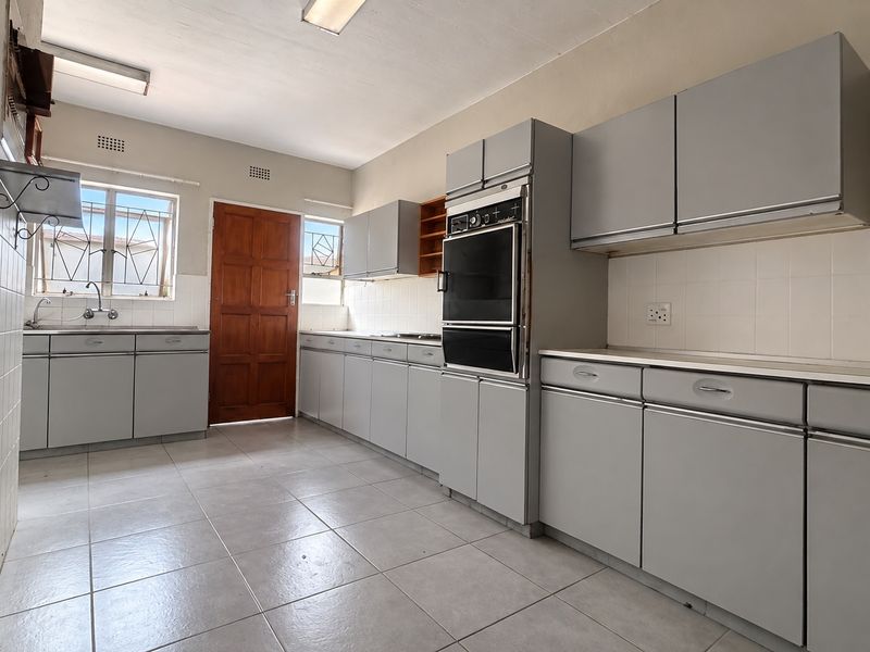 A spacious, empty kitchen featuring built-in grey cabinetry, a double wall oven, tiled flooring, and a tiled backsplash, offering a functional layout for renovation.
