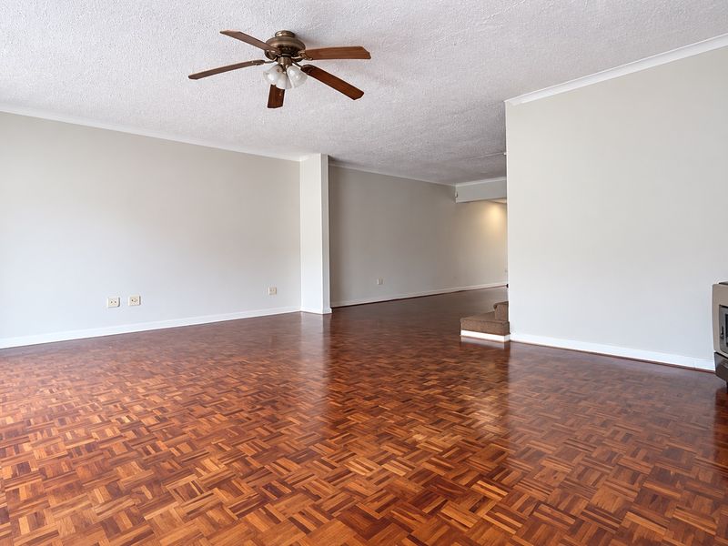 Spacious living area featuring polished parquet flooring, a ceiling fan, and a built-in freestanding fireplace, offering a clean and versatile layout.