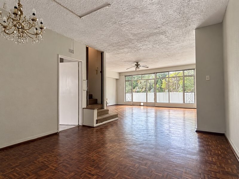 Spacious, empty living area featuring original parquet flooring, a ceiling fan, and large windows that provide ample natural light.