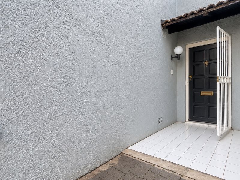 A private townhouse entrance featuring a tiled porch, security gate, and textured exterior wall finish.