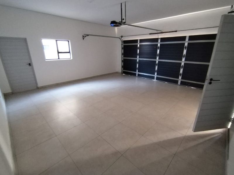 A clean, spacious double garage featuring tiled flooring, a modern sectional door with an automated motor, and convenient internal access.