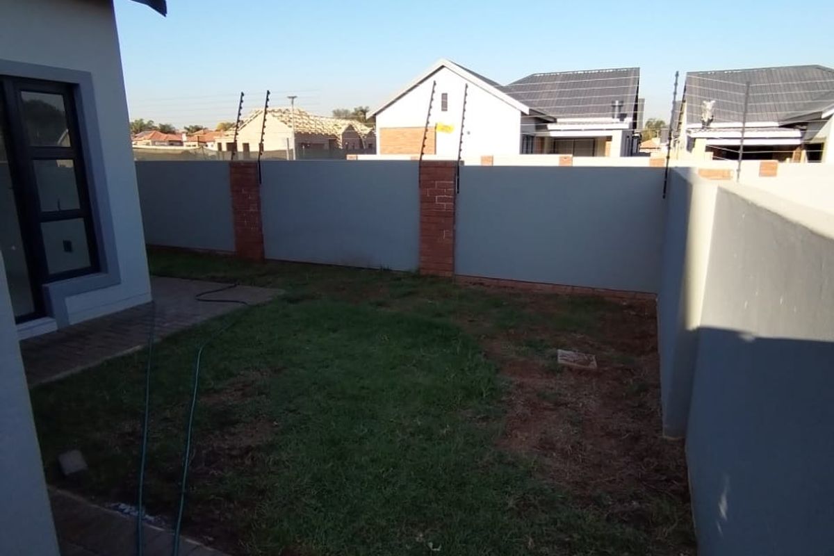 A rear garden area featuring a paved walkway, perimeter wall with electric fencing, and a small lawn space.