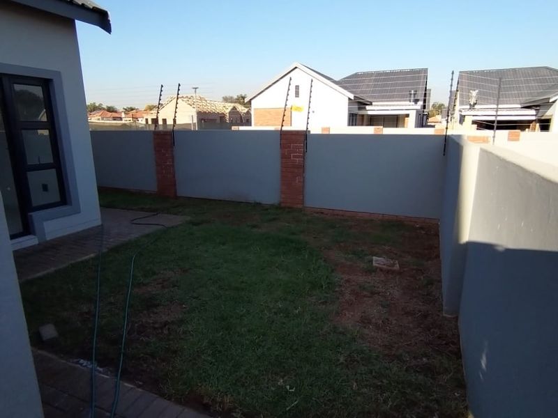 A rear garden area featuring a paved walkway, perimeter wall with electric fencing, and a small lawn space.