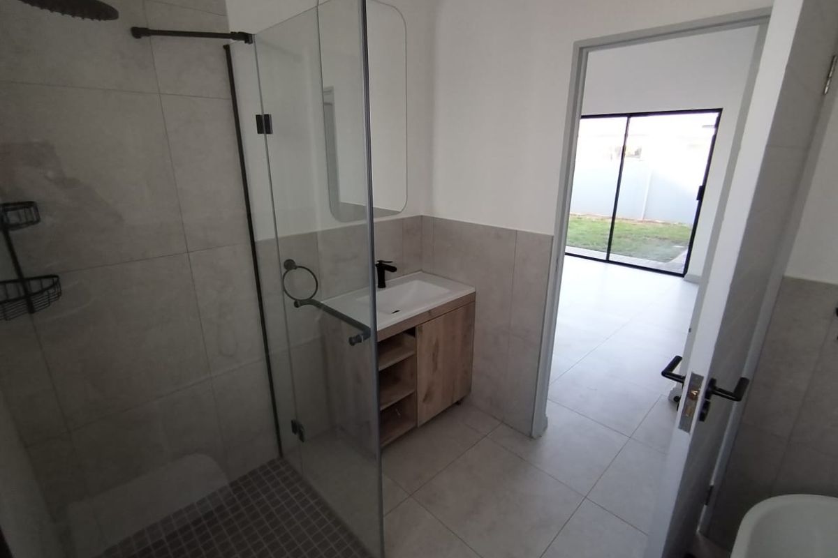 Modern bathroom featuring a walk-in shower with a glass screen, contemporary vanity cabinet, and neutral floor-to-ceiling tiling.