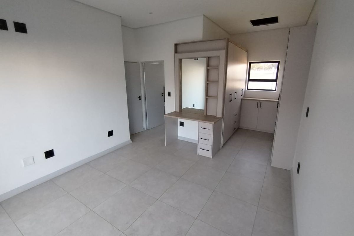 A modern, empty bedroom featuring neutral tiled flooring, built-in cupboards, and a integrated vanity unit with a mirror.