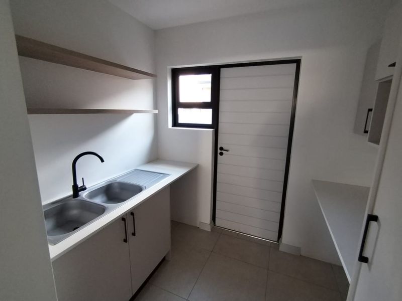 A clean, modern scullery featuring a double bowl stainless steel sink, black mixer tap, built-in cabinetry, and floating shelves with direct external access.