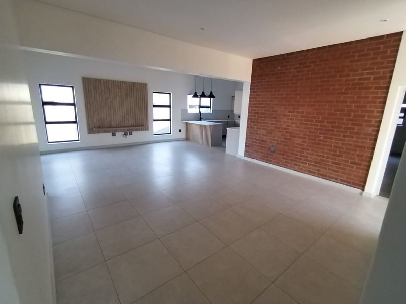 Spacious open-plan living and kitchen area featuring modern tiled floors, an exposed brick feature wall, and contemporary built-in cabinetry.