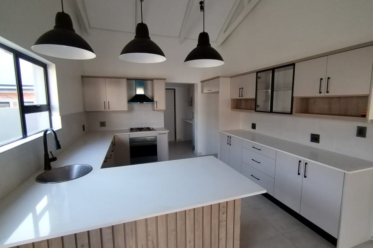 Modern kitchen featuring light wood-tone cabinetry, white quartz countertops, integrated appliances, and stylish pendant lighting under an exposed rafter ceiling.