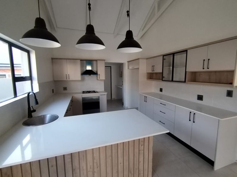 Modern kitchen featuring light wood-tone cabinetry, white quartz countertops, integrated appliances, and stylish pendant lighting under an exposed rafter ceiling.