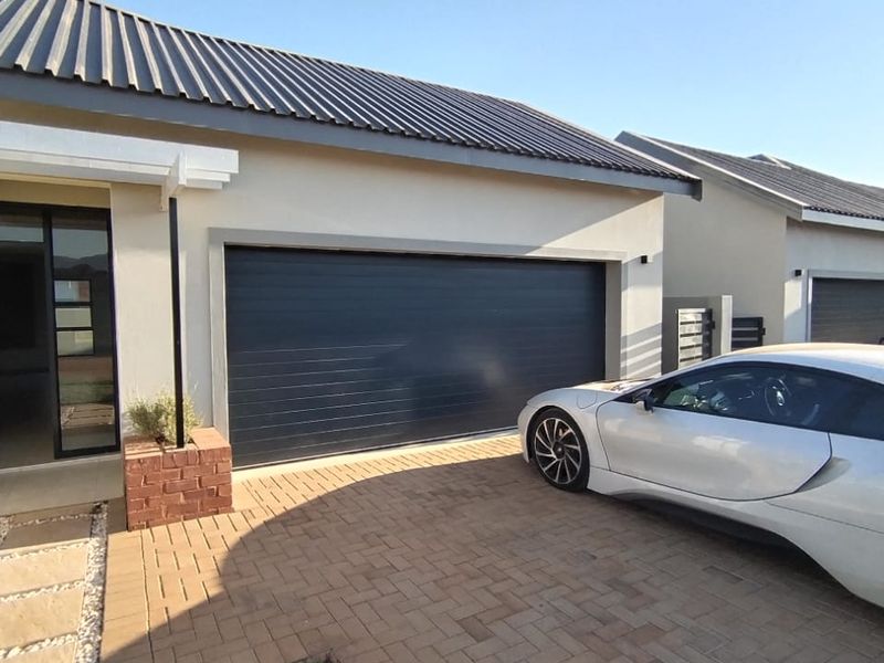 Front exterior view of the property featuring a modern sectional garage door, brick paved driveway, and a neat entrance area.