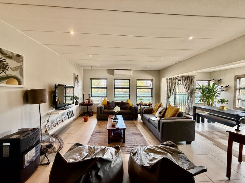 Spacious open-plan living and dining area featuring tiled flooring, recessed lighting, and a wall-mounted air conditioning unit with large windows for natural light.