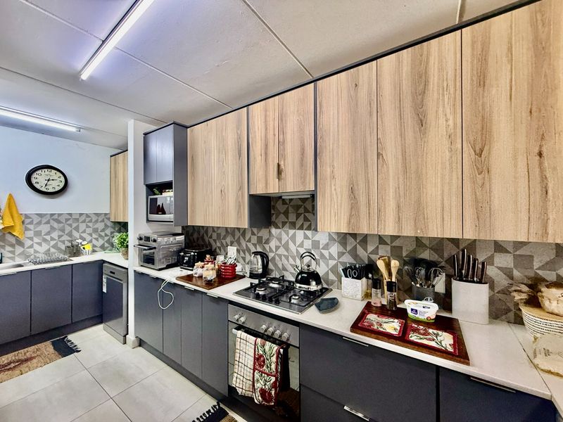 Modern kitchen featuring two-tone cabinetry, stone countertops, a gas hob, built-in oven, and a stylish geometric tile backsplash.