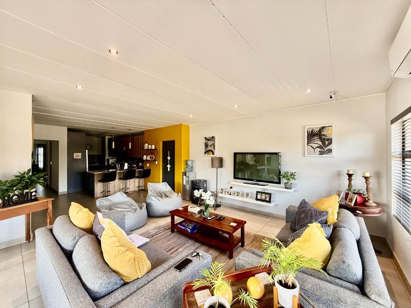 Spacious open-plan living area featuring a modern kitchen with island seating, tiled floors, recessed lighting, and a dedicated media wall with floating shelving.