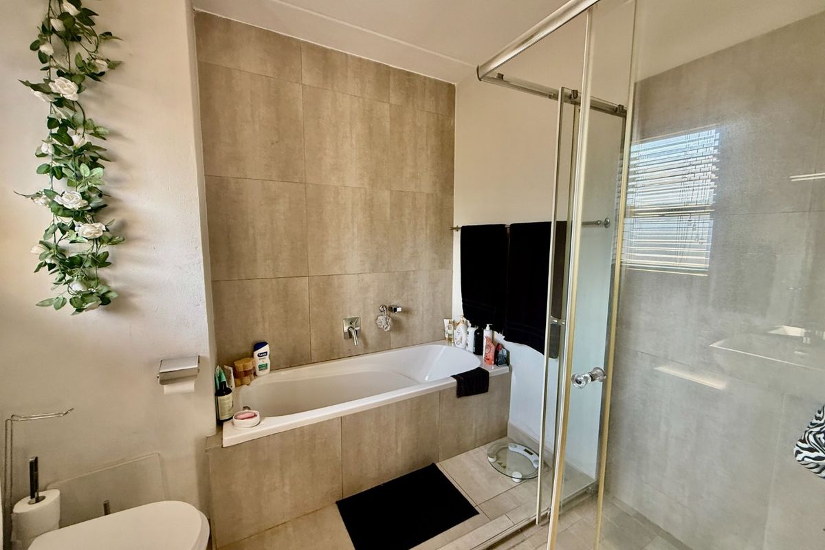 Modern bathroom featuring a built-in bathtub with tiled surround, a separate glass-enclosed shower, and neutral floor-to-ceiling wall tiling.