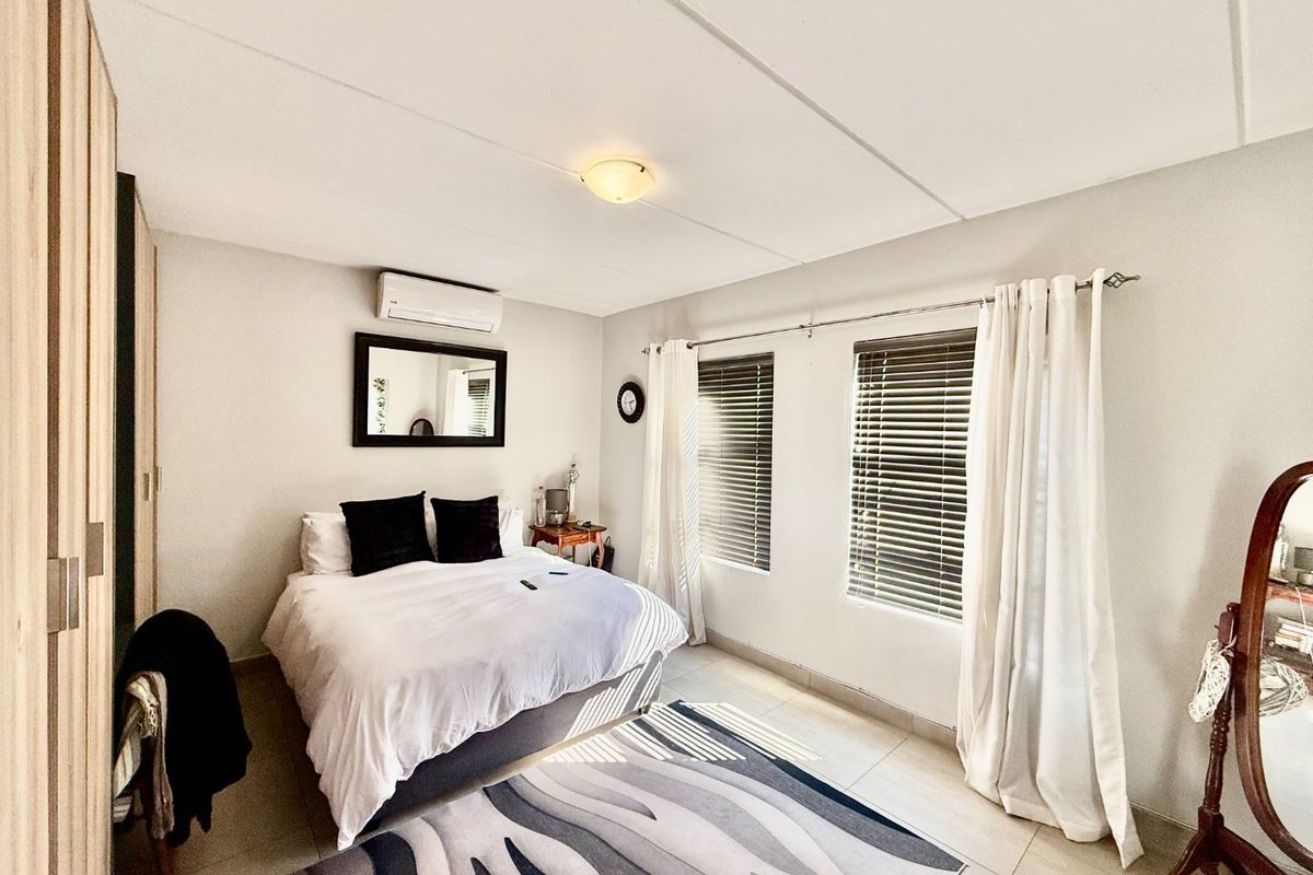 A well-maintained bedroom featuring tiled flooring, a built-in wardrobe, and a wall-mounted air conditioning unit with natural light through venetian blinds.