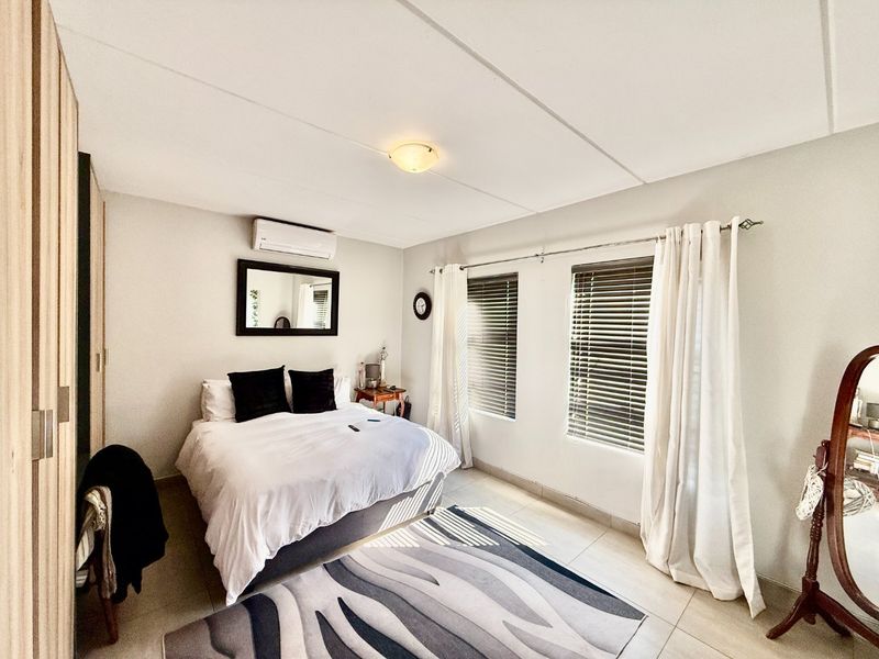 A well-maintained bedroom featuring tiled flooring, a built-in wardrobe, and a wall-mounted air conditioning unit with natural light through venetian blinds.