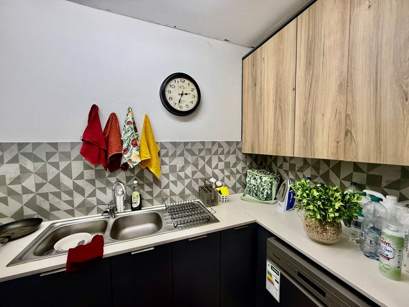 A functional kitchen featuring wood-look upper cabinets, dark lower cabinetry, a double stainless steel sink, and a modern geometric tile splashback.