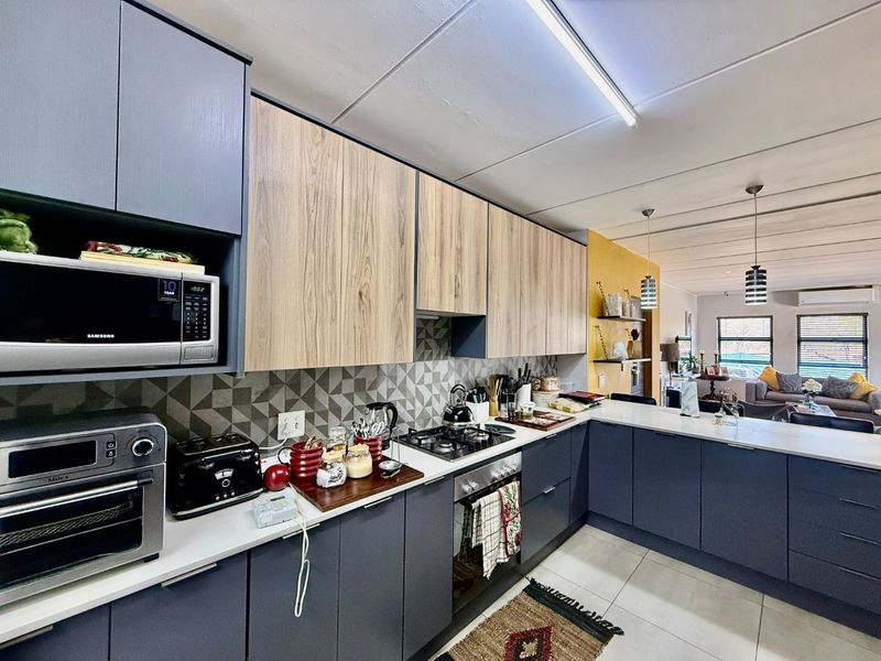 Modern open-plan kitchen featuring two-tone cabinetry, stone countertops, geometric backsplash, and integrated appliances, flowing seamlessly into the adjacent living area.