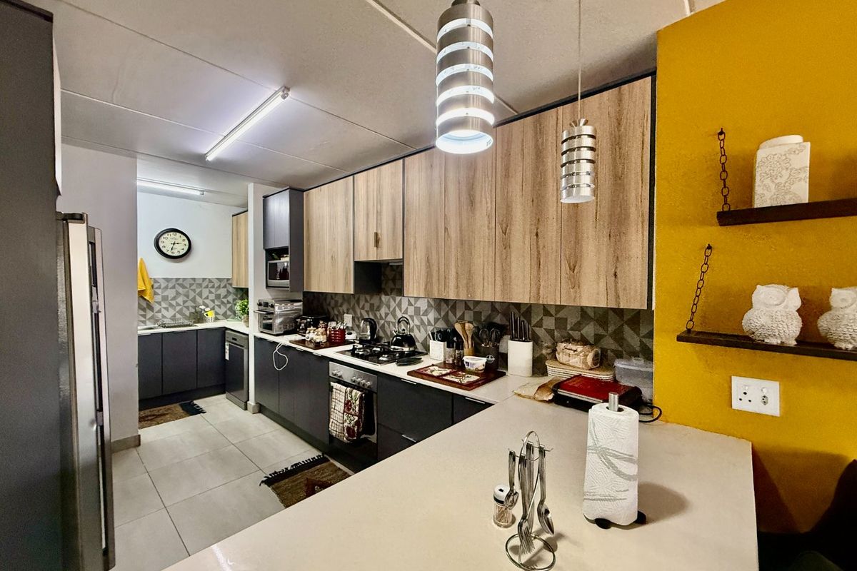 Modern kitchen featuring wood-grain and dark cabinetry, stone countertops, gas hob, built-in oven, and stylish pendant lighting with a tiled backsplash.