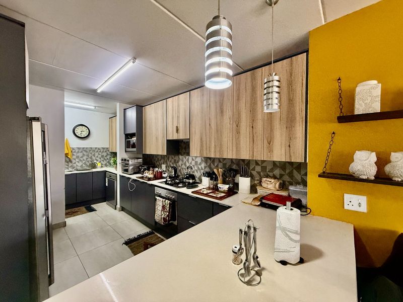 Modern kitchen featuring wood-grain and dark cabinetry, stone countertops, gas hob, built-in oven, and stylish pendant lighting with a tiled backsplash.