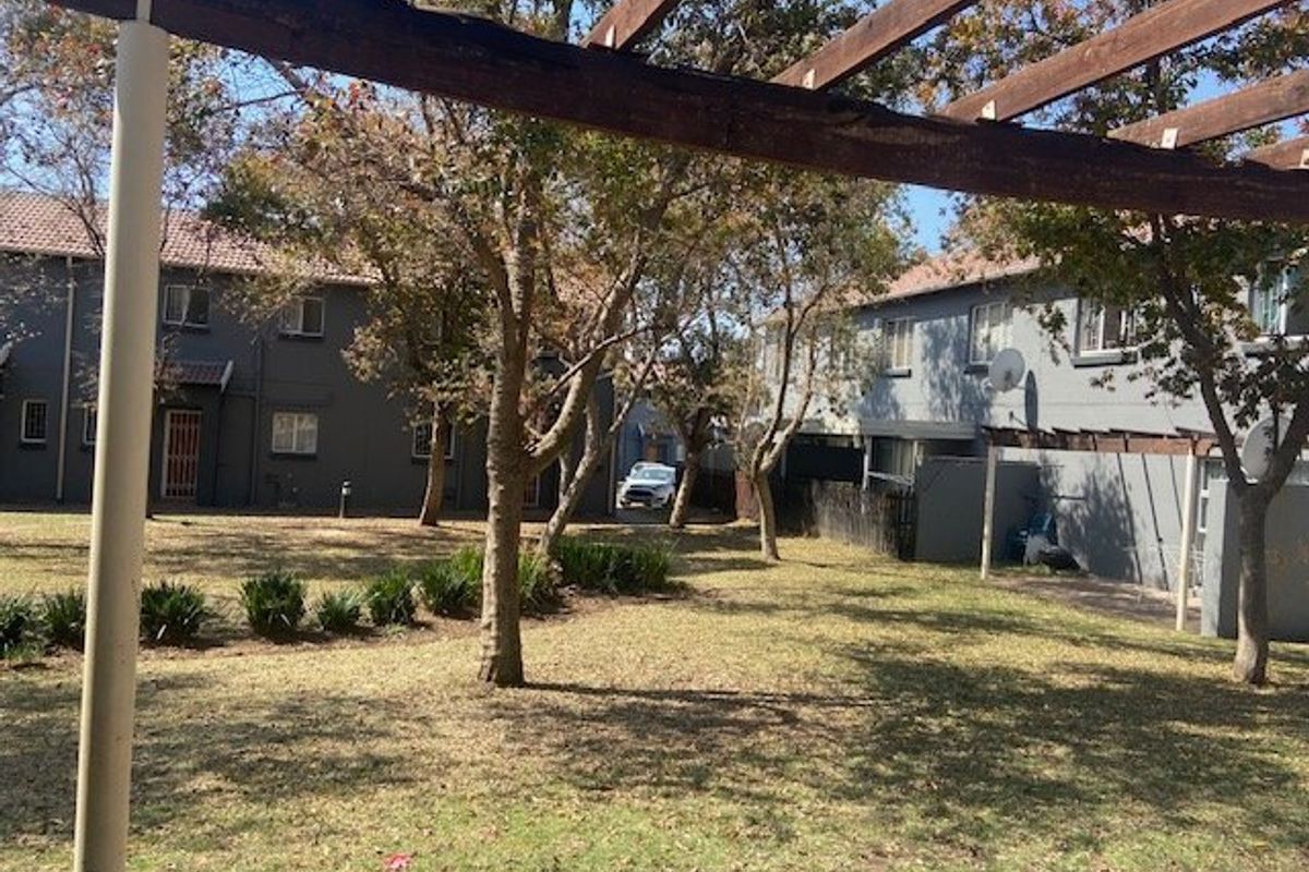A view of the rear communal garden area featuring a wooden pergola structure and established trees between townhouse units.