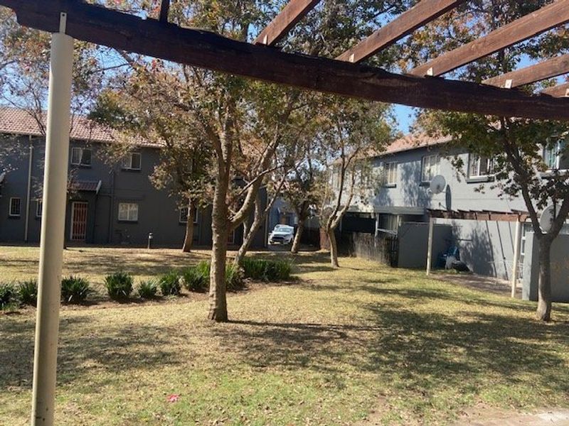 A view of the rear communal garden area featuring a wooden pergola structure and established trees between townhouse units.