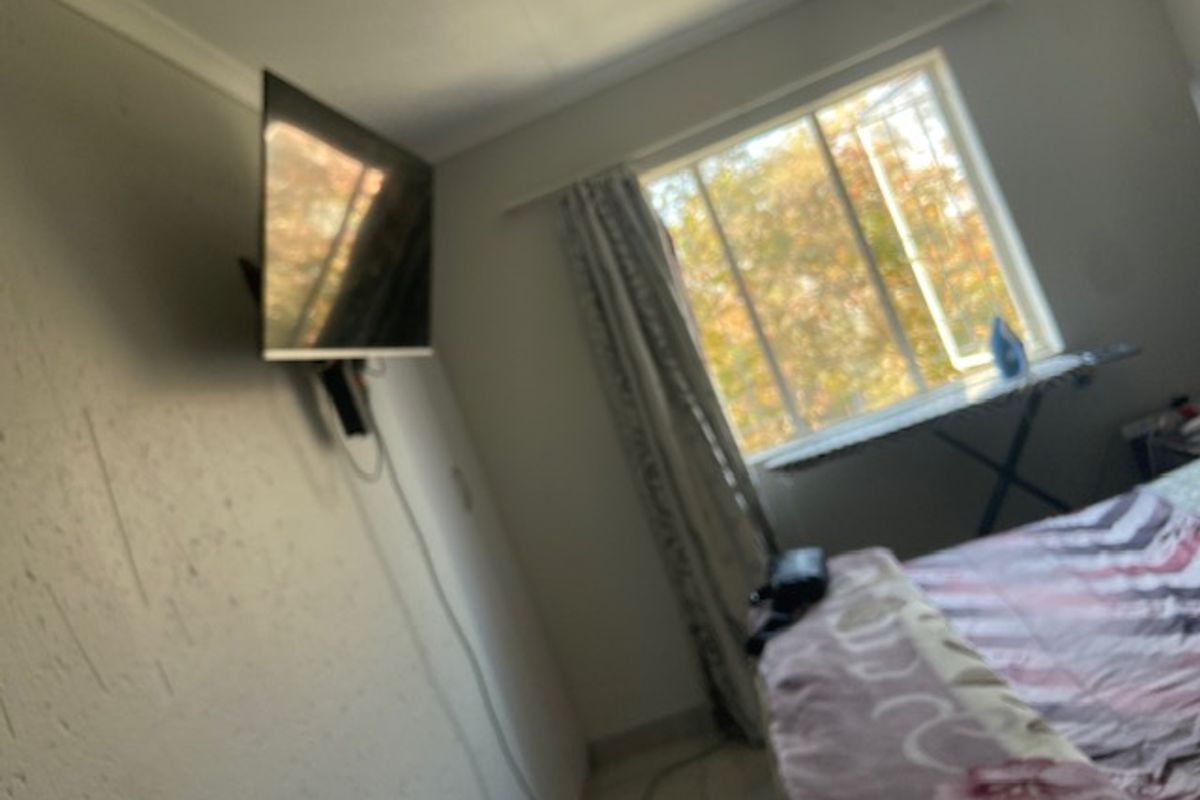 A bedroom featuring a sliding window and wall-mounted television bracket, currently showing signs of wear on the wall surfaces.