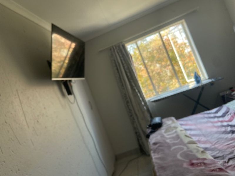 A bedroom featuring a sliding window and wall-mounted television bracket, currently showing signs of wear on the wall surfaces.