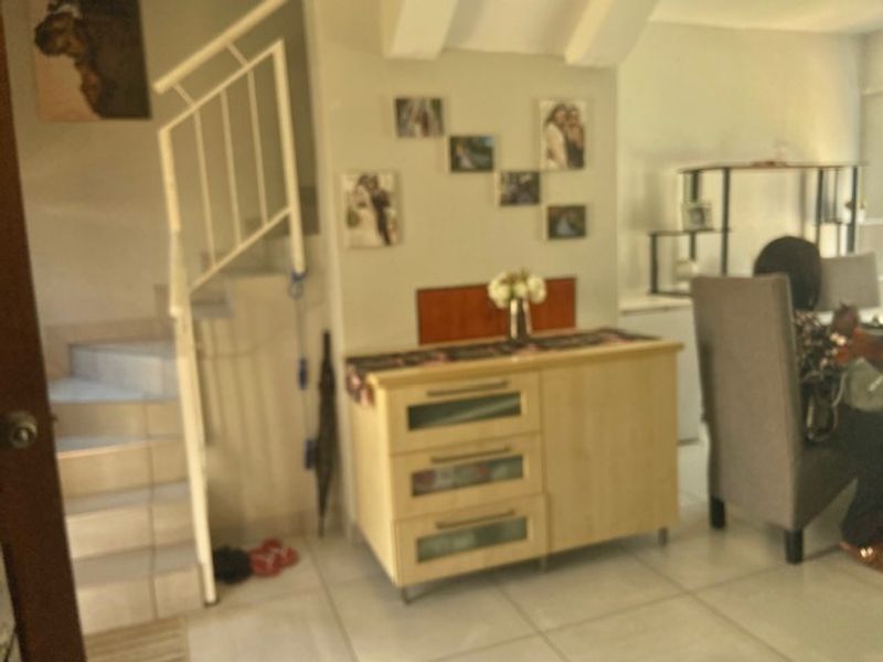 A living area featuring tiled flooring and an internal staircase with a metal balustrade, providing access to the upper level of the townhouse.