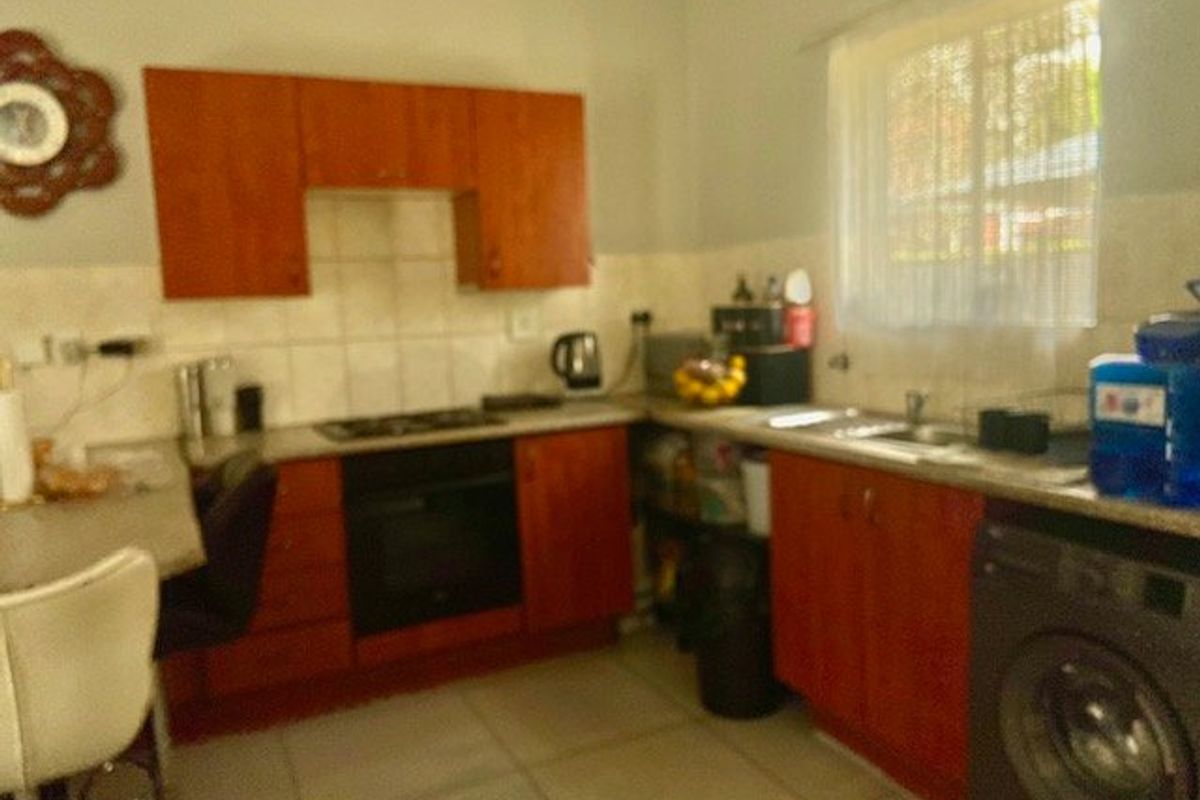 A functional kitchen featuring wooden cabinetry, tiled backsplash, built-in oven, hob, and integrated sink area with tiled flooring.